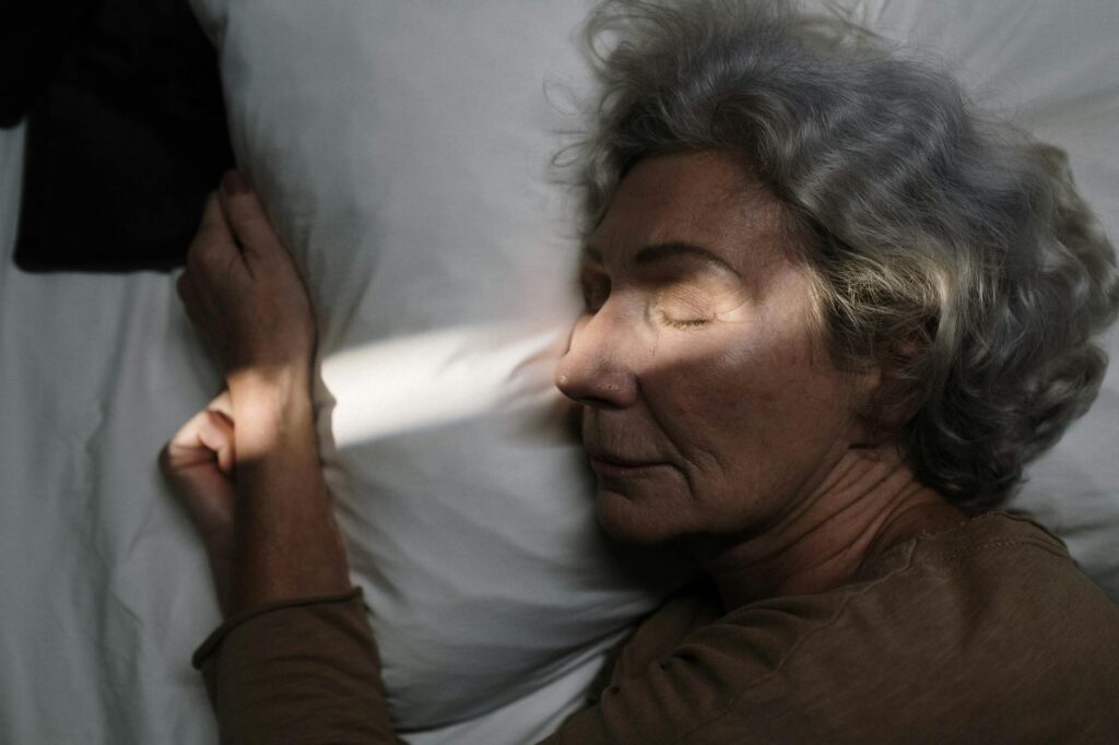 Serene image of elderly woman resting peacefully on pillow with sunlight grazing her face.